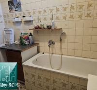 A bathroom with a bathtub in a family house, tiled with floral-patterned tiles.