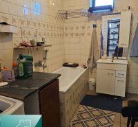 Bathroom in a family house with a bathtub, cabinet, and tiles on the walls.