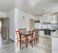 A kitchen in a family house with ceramic tiles, a wooden table, and white cabinets.