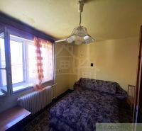 A room in a family house with a sofa, a window, and curtains in warm colors.