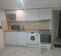 A kitchen in a one-room apartment with white kitchen cabinets and a wooden decor floor.