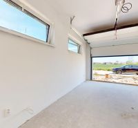 A garage in a family house with open doors, a view of the car and greenery.