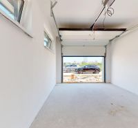 An empty garage in a family house with open doors, cars outside.
