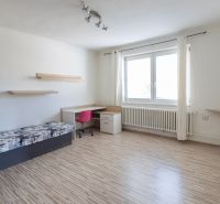 A room in a family house with a bed, a table, a pink chair, and a floor with a wooden decor.