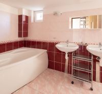 A bathroom in a family house with a corner bathtub and two sinks on pink-red tiles.