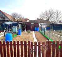 A garden in Hlboké with rural buildings and barrels between fences.