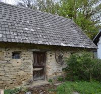 A stone barn next to a family house in Bukovec with wooden doors and a tiled roof.