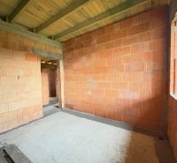 An unfinished interior of a family house with brick walls and a wooden beam ceiling.