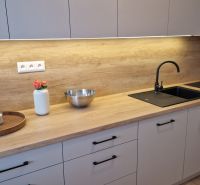 A kitchen in a 3-room apartment with a wooden decor floor, light cabinets, and a black sink.
