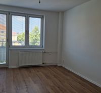 A room in a 3-room apartment with a wooden decor floor, a large window, and a radiator.