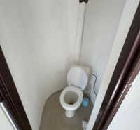 Simple toilet in a cabin with a wall without tiles and a plastic toilet.