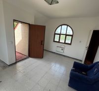 A room in a cottage with doors to the terrace, a tiled floor, and a dark blue armchair.