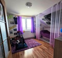 Children's room with purple curtains, carpet, bed, wooden decor flooring.