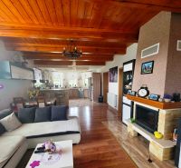 Living room with kitchen, fireplace, and wooden decor flooring in a family house.