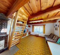Living room in a family house with a tiled stove, wooden ceilings, and a ladder to the upper floor.
