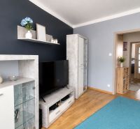 Living room in a 3-room apartment with shelves, a television, and a wooden decor floor.