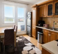 A kitchen in a 3-room apartment with wooden cabinets, a dining table, and a large window.