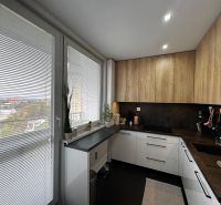 A kitchen in a 3-room apartment with a wooden decor floor, white blinds, and a view.