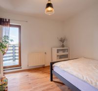 A bright bedroom in a 4-room apartment with wood-patterned flooring, a plant, and a balcony.