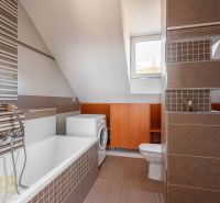 A bathroom with a pitched roof, a bathtub, a washing machine, and brown tiles in a 4-room apartment.