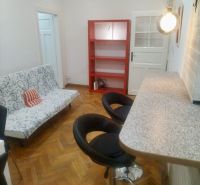 Living room with a bar counter, sofa, and shelves in a two-room apartment with a wooden decor floor.