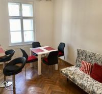 Living area in a two-room apartment with a wood-patterned floor and a dining table.
