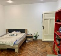 Bedroom in a 2-room apartment with a bed, red shelf, and wooden decor flooring.