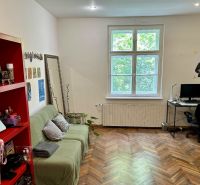 Living room in a two-room apartment with a wood-patterned floor, a sofa, and a computer desk.