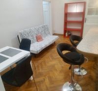 Living room of a two-room apartment with a wooden decor floor, a dining table, and bar stools.