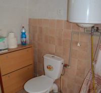 Bathroom in a family house with a toilet, furniture, a bottle, and a water heater.