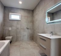 A bathroom in a family house with a bathtub, shower, ladder radiator, and backlit mirror.