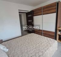 A bedroom with a wood-patterned floor, a built-in wardrobe, and a bed in a three-room apartment.