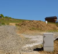 Recreational plots in Nová Kelča, gravel road, wooden house, slopes and vegetation.