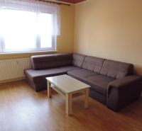 A bright living room in a two-room apartment with a sofa and a table on a wooden-decorated floor.