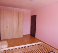 A room in a 2-room apartment with pink walls, a wardrobe, and a floor with a wooden decor.