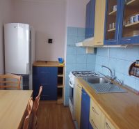 Kitchen area in a 2-room apartment with chairs, wooden decor flooring, blue tiles.