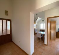 A hallway in a vacation apartment with a ceramic floor, a dining area, and a room in the background.