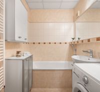 A bathroom in a 3-room apartment with a bathtub, washing machine, and cabinet.
