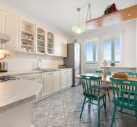 A kitchen in a 3-room apartment with a gas stove and a dining table with green chairs.