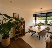 A dining room in a family house with wooden decor, plants, and a large window.