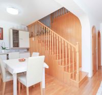 Dining room with staircase, wooden decor flooring, light chairs and table in a family house.