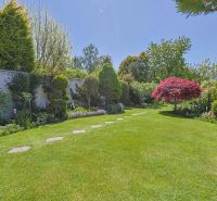 A garden with a manicured lawn and colorful trees by a family house.