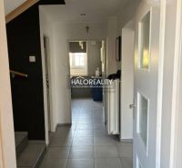 A hallway of a family house with white walls, tiles, and a view of the kitchen.