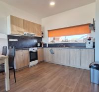 A kitchen in a family house with a corner unit, a dining table, and a floor with a wooden decor.