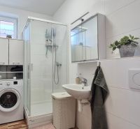 A bathroom in a family house with a washing machine, a shower corner, and a white sink.
