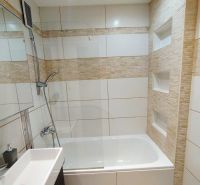 A bathroom in a one-room apartment with a bathtub, shower, and ceramic tiles on the walls.