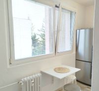 A kitchen in a studio apartment with a window, a refrigerator, and a small table for seating.