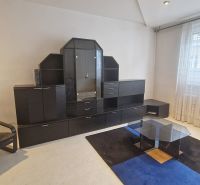 Living room with a sofa, glass table, and dark wall unit in a 3-room apartment.