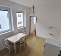 A dining room with a wooden table and chairs in a 3-room apartment, with two windows and light.