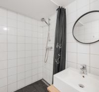 A bathroom with white tiles, a shower, and a sink in a two-room apartment.